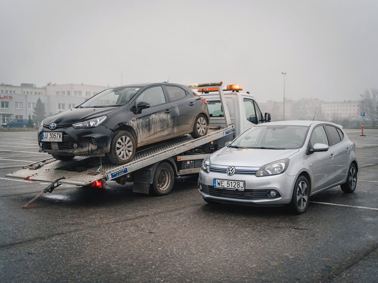 Logistyka — odbiór auta i pojazd zastępczy Odbiór auta lawetą i auto zastępcze — uszkodzony samochód wjeżdża na lawetę, obok czeka pojazd tej samej klasy